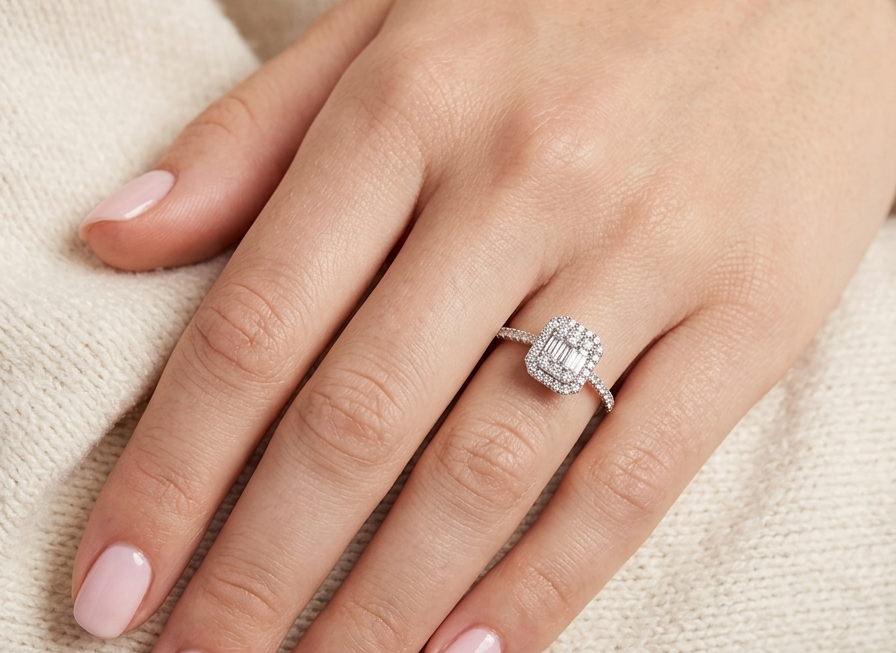 hand A rectangular diamond cluster ring. Centre portion is set with three baguette cut white diamonds 3x1.6mm and six mixed cut diamonds 2mm each.
Surrounded by a halo of twenty two small round diamonds
