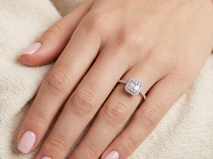 hand A rectangular diamond cluster ring. Centre portion is set with three baguette cut white diamonds 3x1.6mm and six mixed cut diamonds 2mm each.
Surrounded by a halo of twenty two small round diamonds