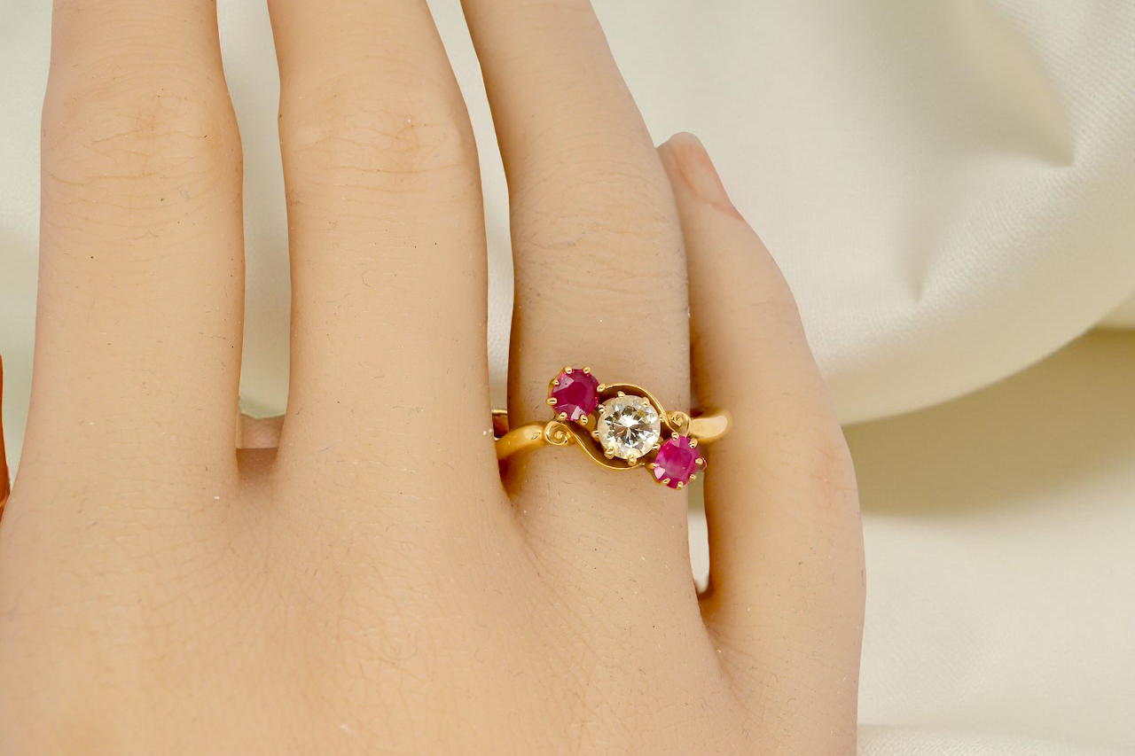 Gold ring with red gemstones on a person's finger against a neutral background