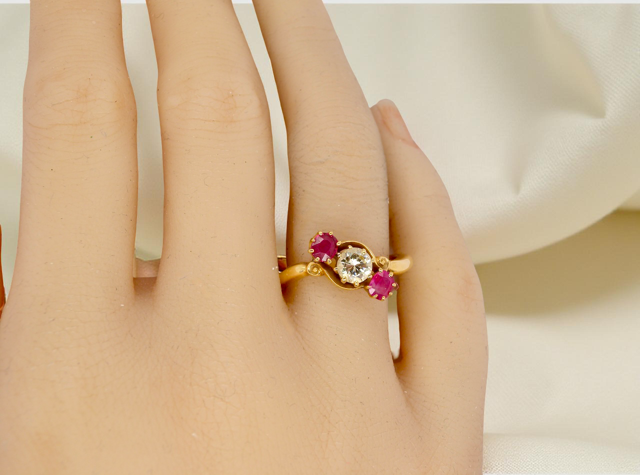 Gold ring with red gemstones on a person's finger against a neutral background