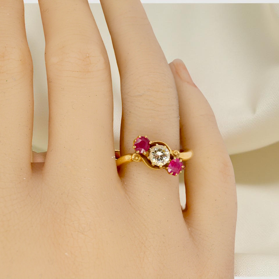 Gold ring with red gemstones on a person's finger against a neutral background