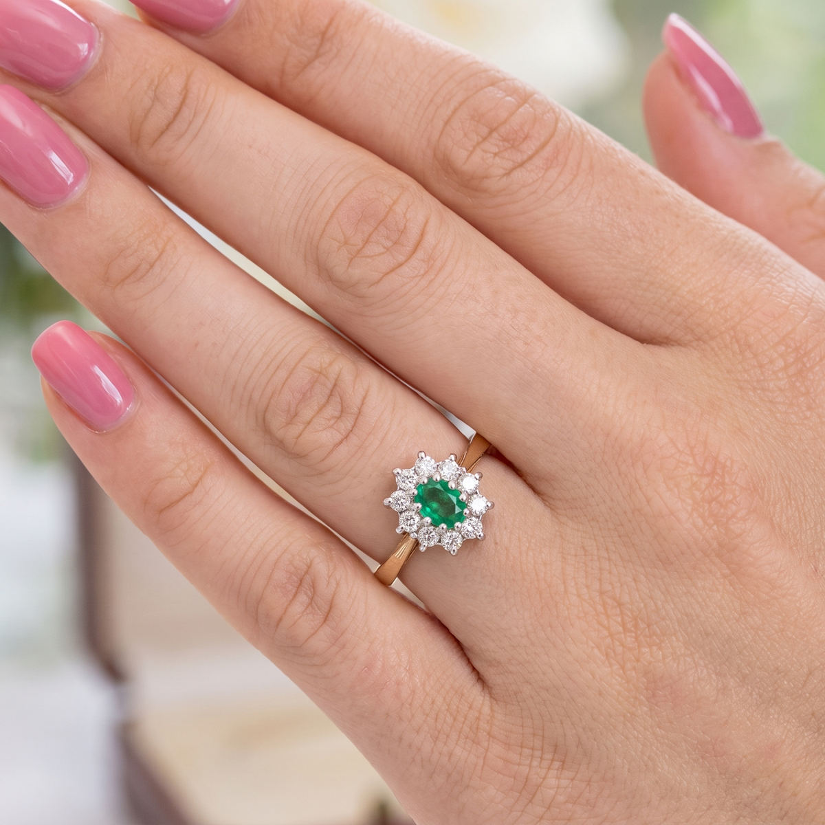 hand A traditional cluster ring. Features to the centre an oval shaped emerald, 5.5x4.5mm (est 0.35 carats) deep green colour. 