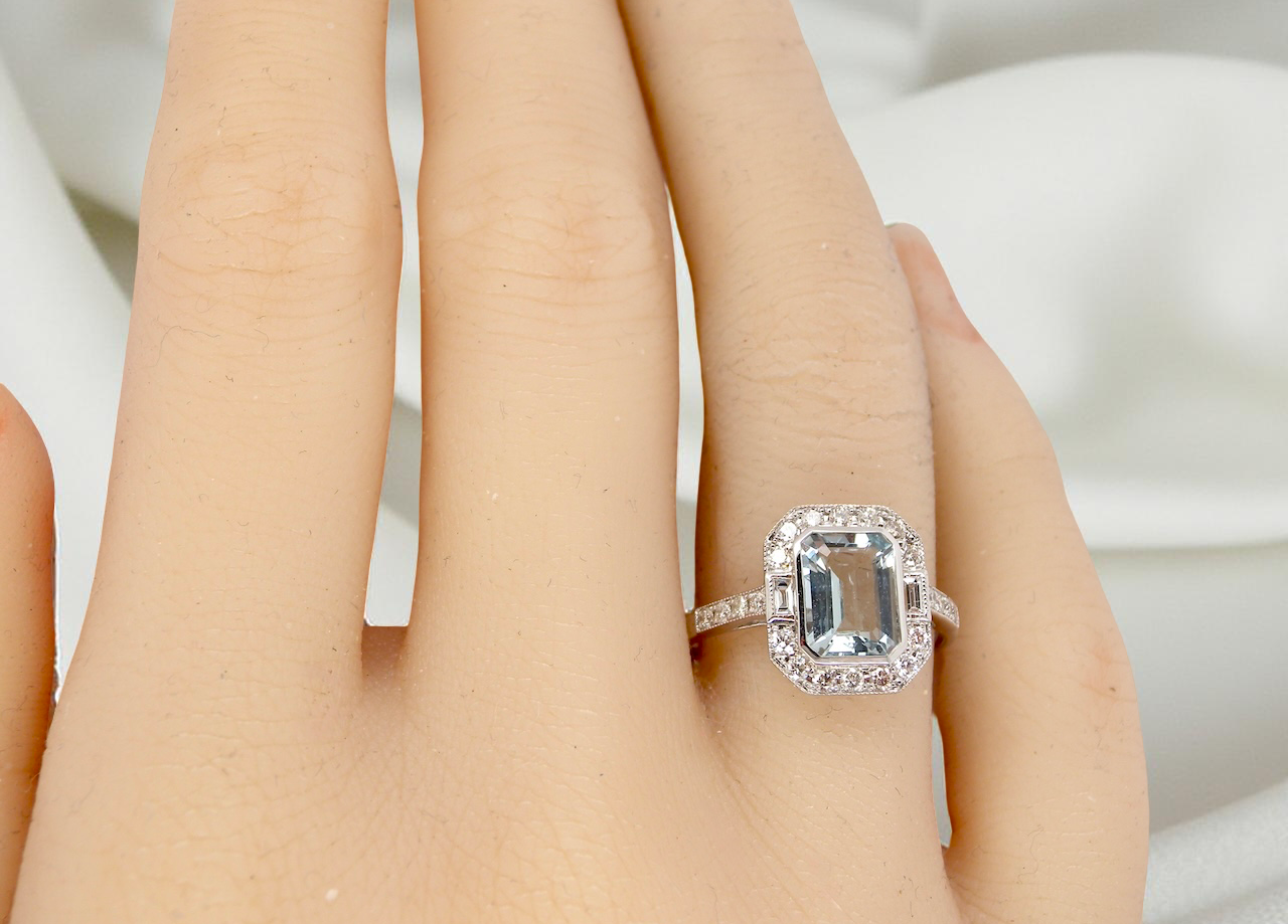 hand A very pretty cluster ring. Features a step cut aquamarine centre stone, 8x7mm (est 1.21 carats). Plain rim setting.