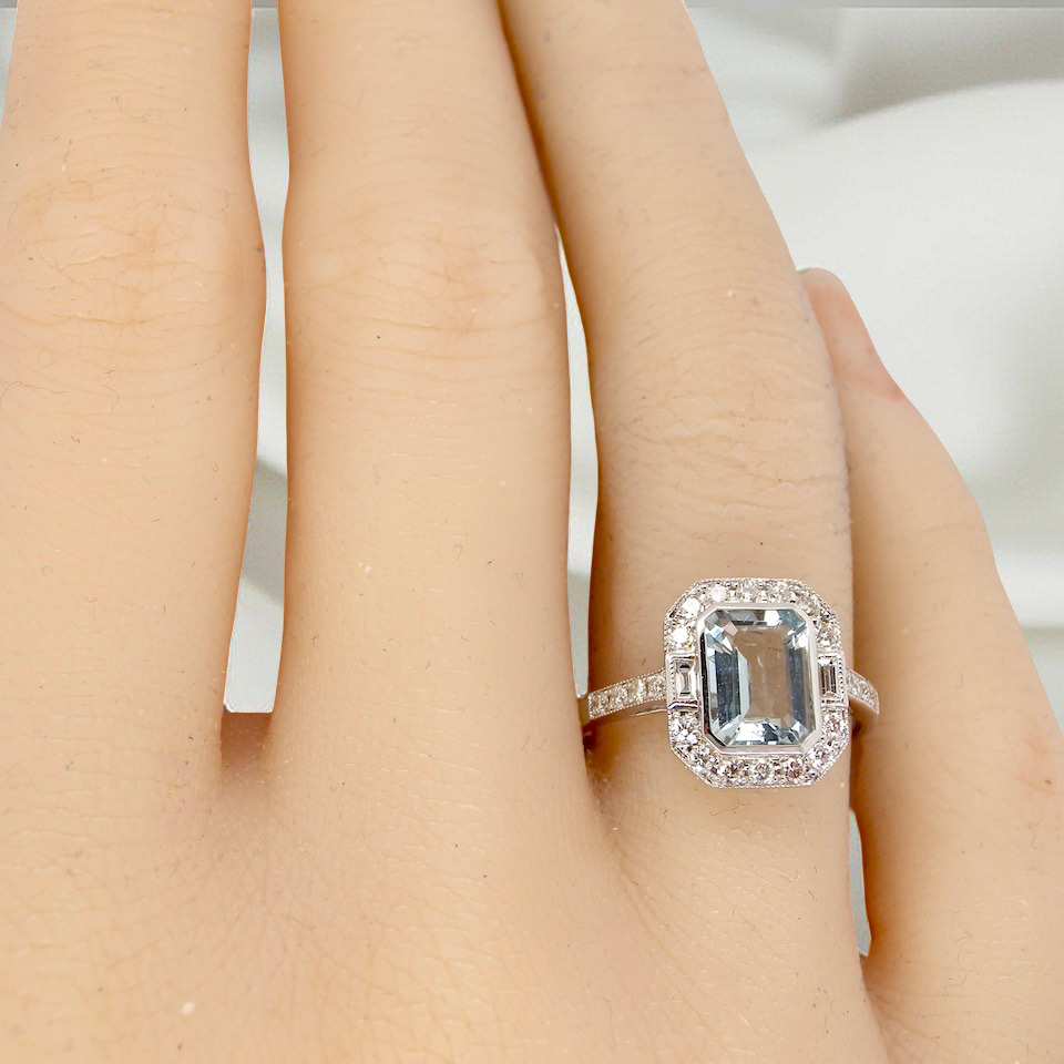 hand A very pretty cluster ring. Features a step cut aquamarine centre stone, 8x7mm (est 1.21 carats). Plain rim setting.