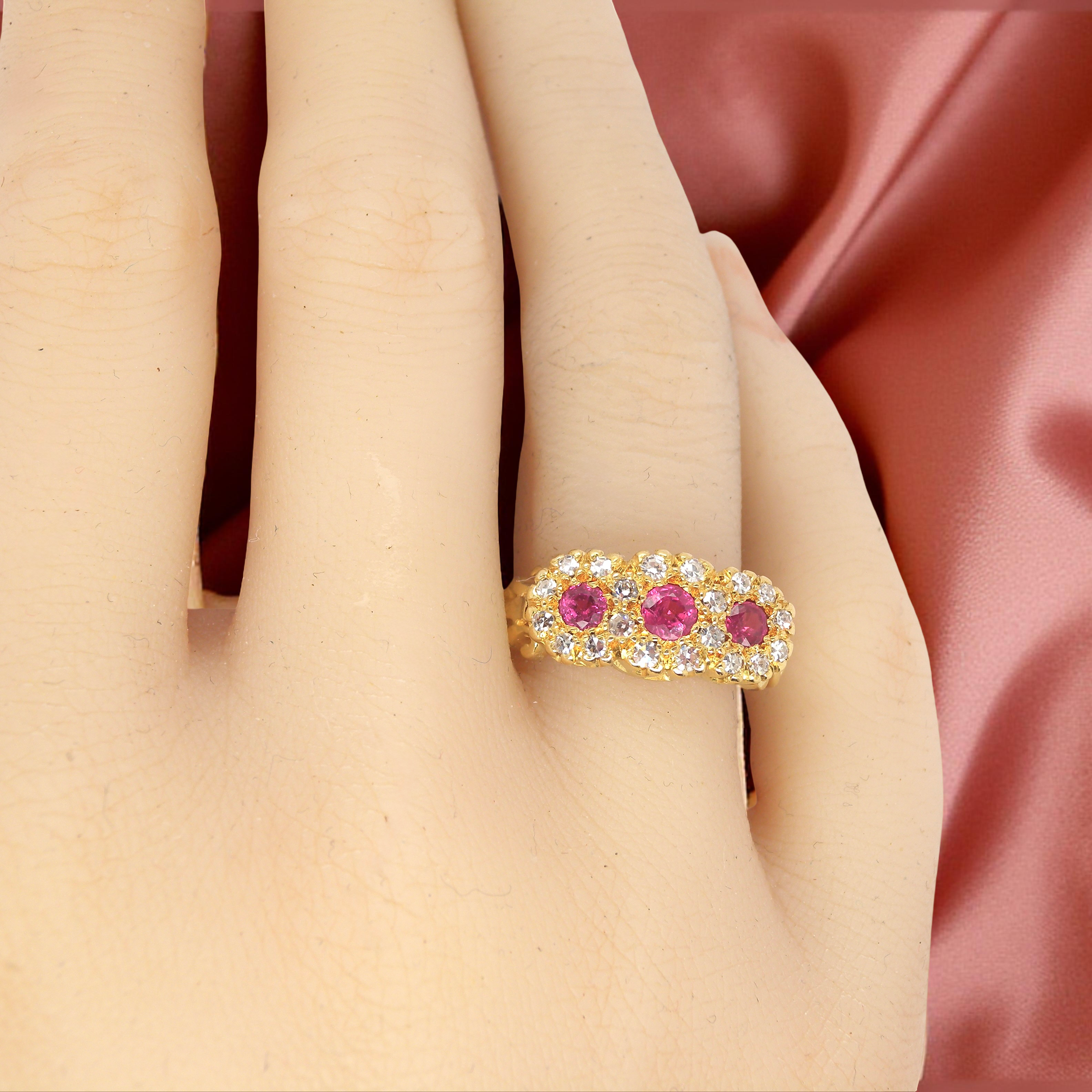 Gold ring with pink gemstones on a hand against a pink satin background