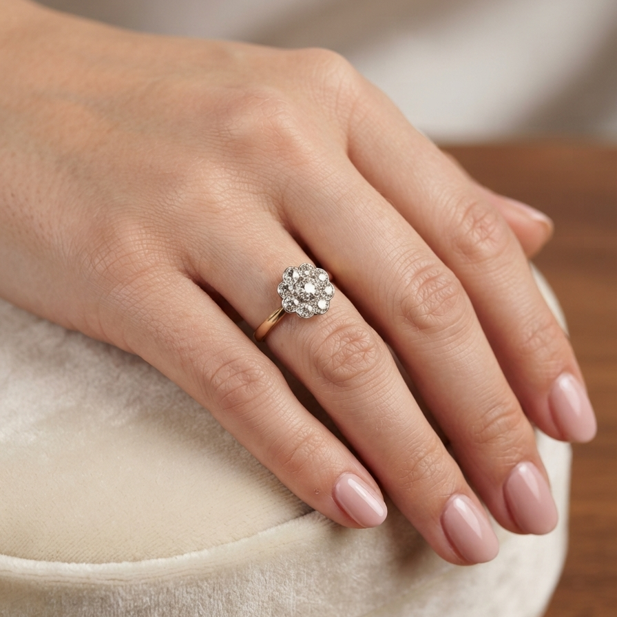 A close-up of a hand wearing a rose gold ring with a diamond cluster setting, resting on a cream velvet ring box.