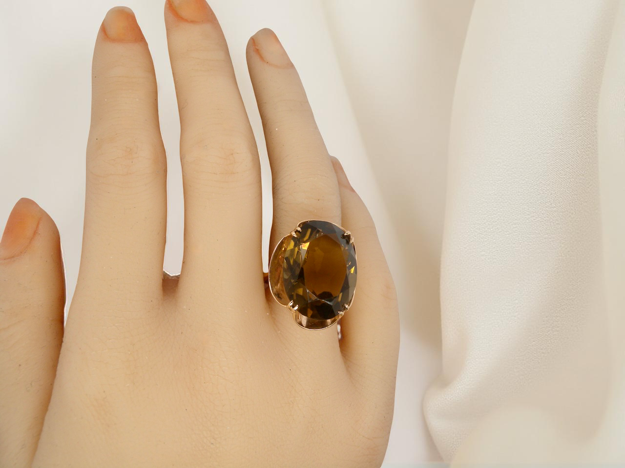 Gold ring with a large gemstone on a hand against a white background