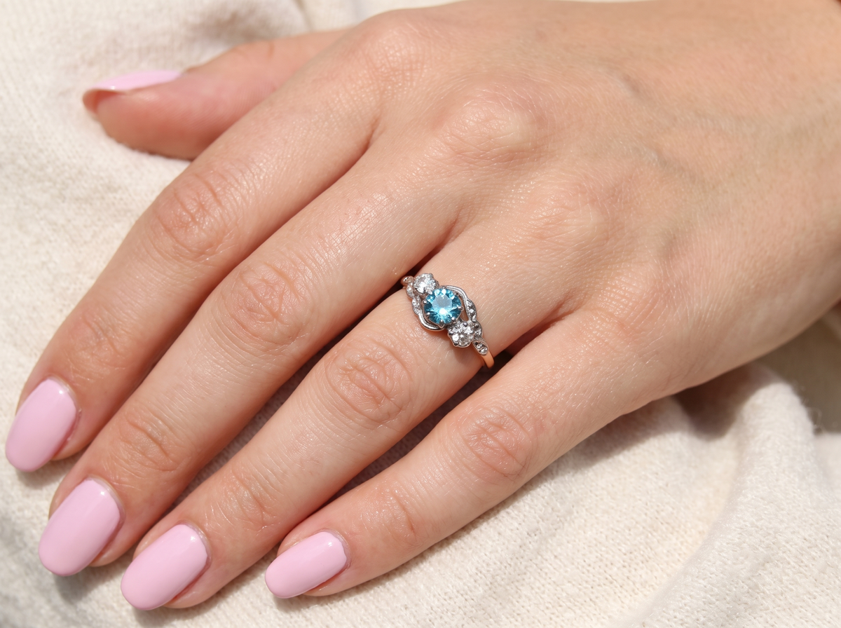 hand A vintage three stone ring, cross over style and features a round 6mm natural blue zircon centre stone