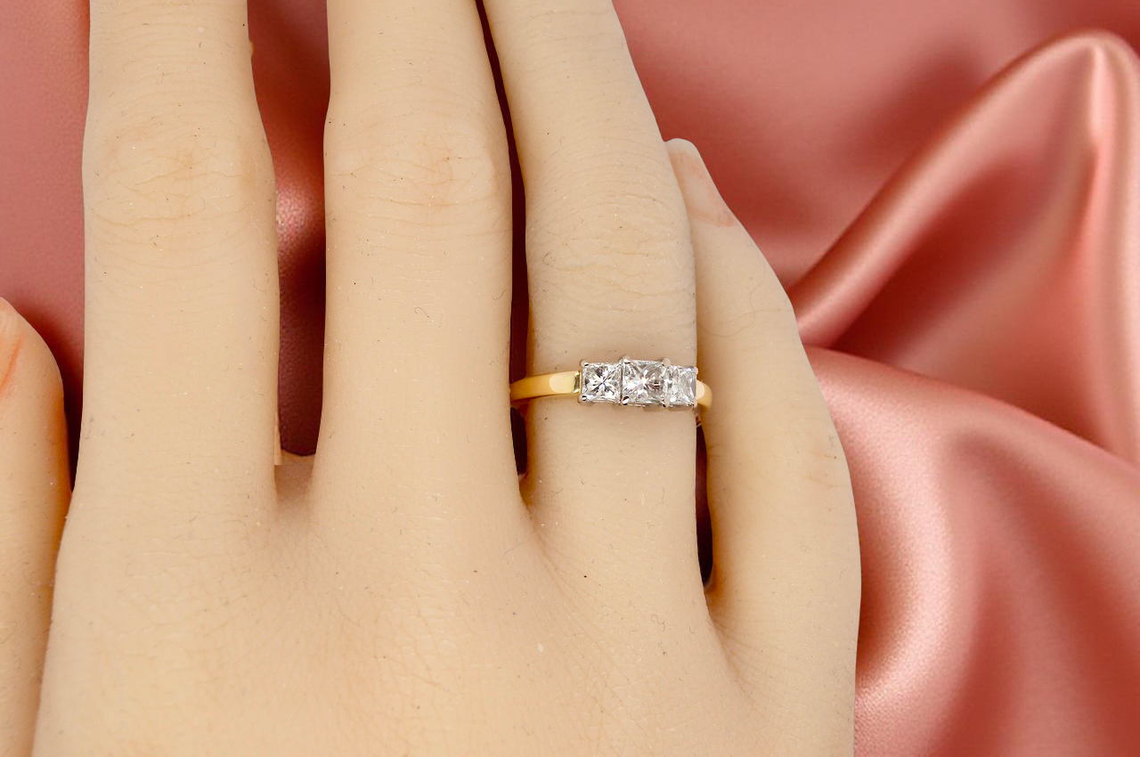 Gold ring with diamonds on a hand against a pink satin background