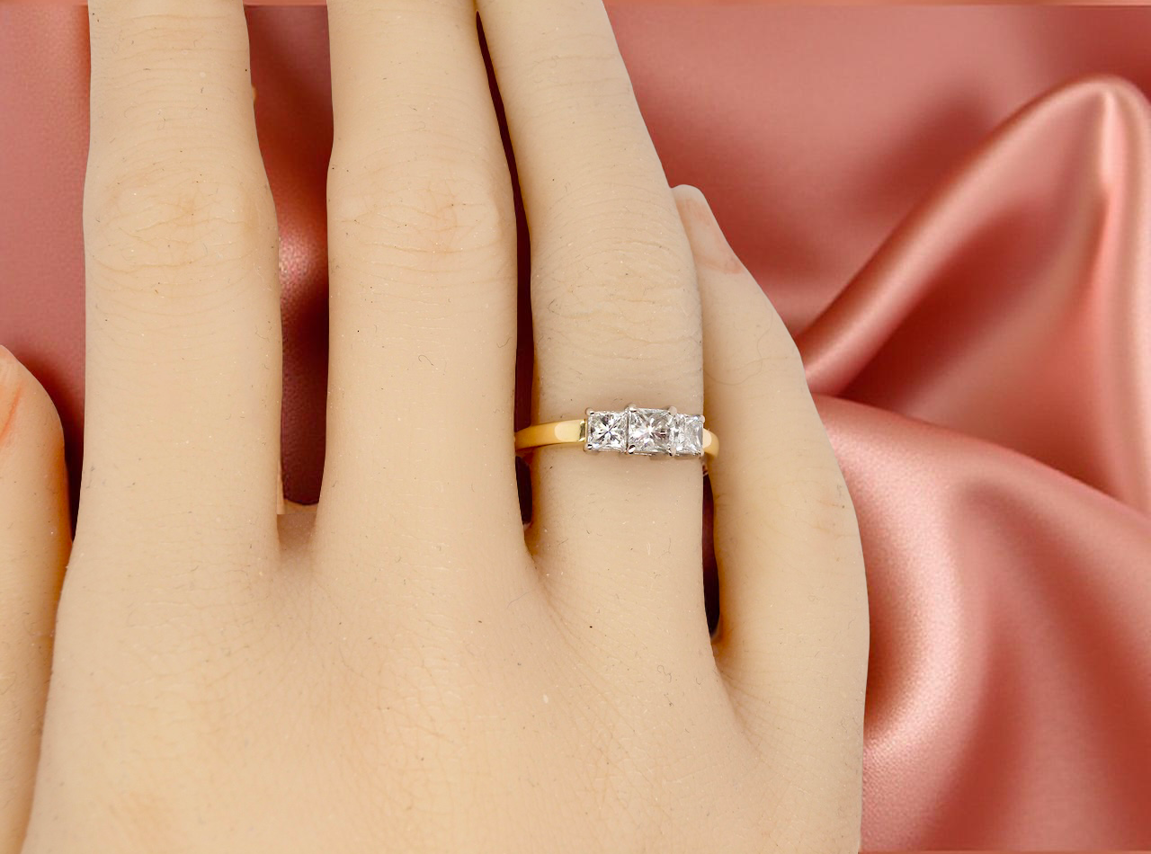 Gold ring with diamonds on a hand against a pink satin background