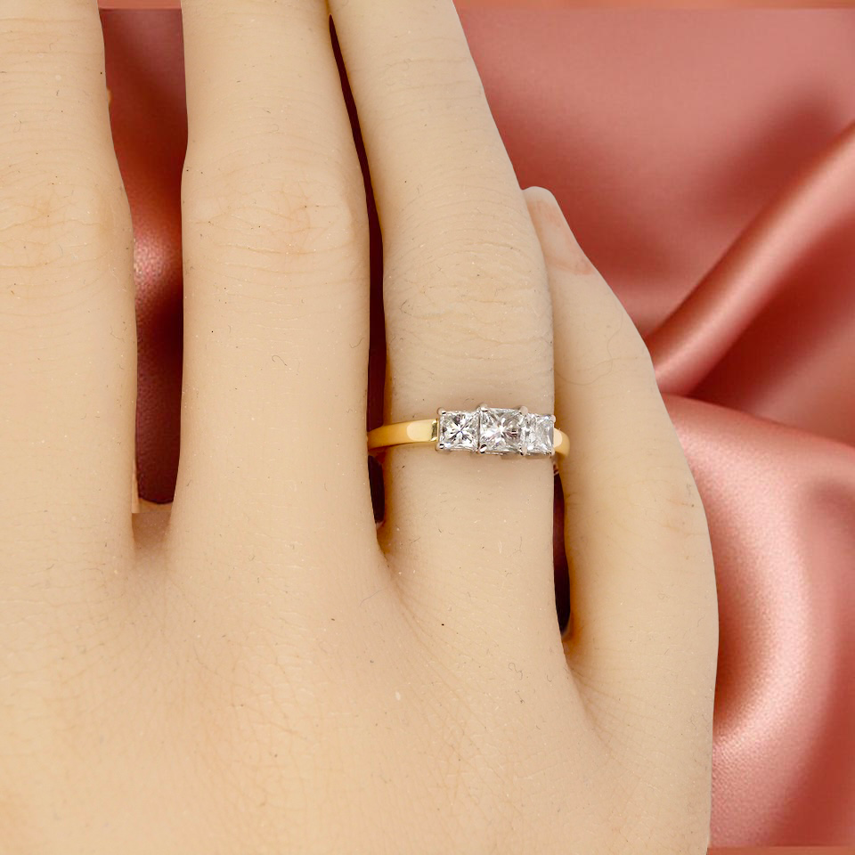 Gold ring with diamonds on a hand against a pink satin background