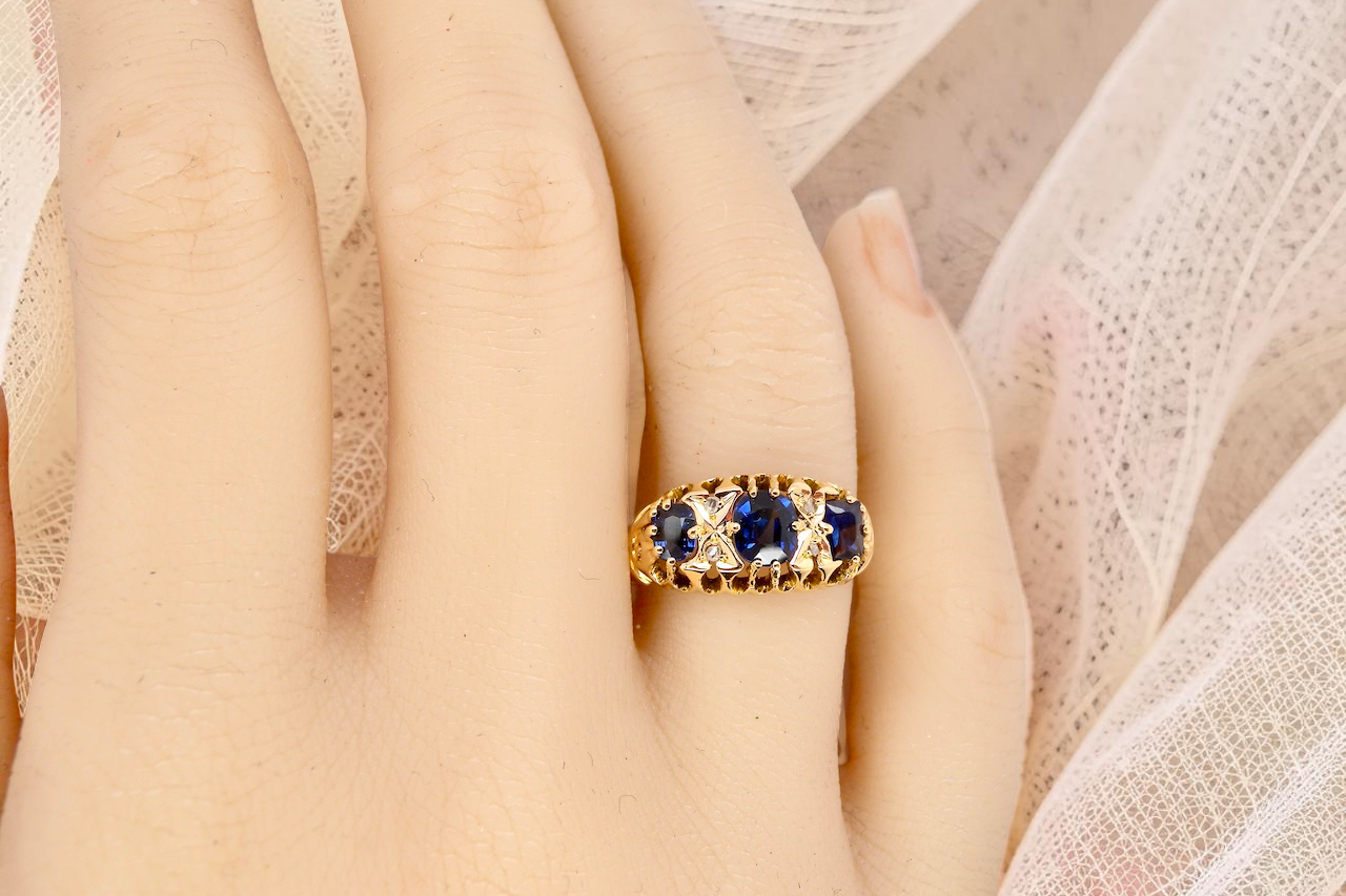 hand An 18 carat gold antique boat shaped ring. Features three oval to cushion cut sapphires, centre 6x5mm, each end 5x3mm. Mid to dark blue