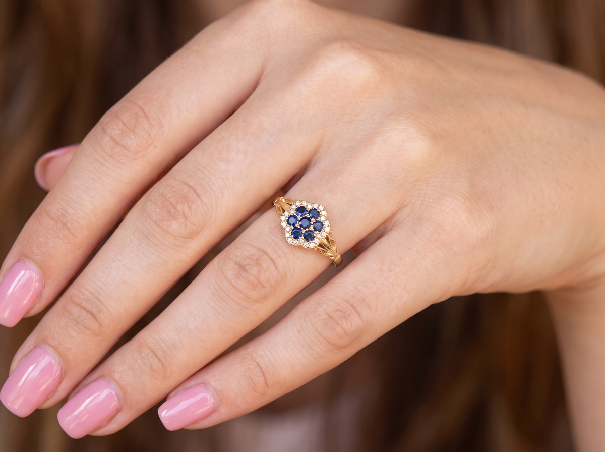 hand An 18 carat gold cluster ring. The centre a floral combination of seven sapphires, each 2.5mm, mid to dark blue.