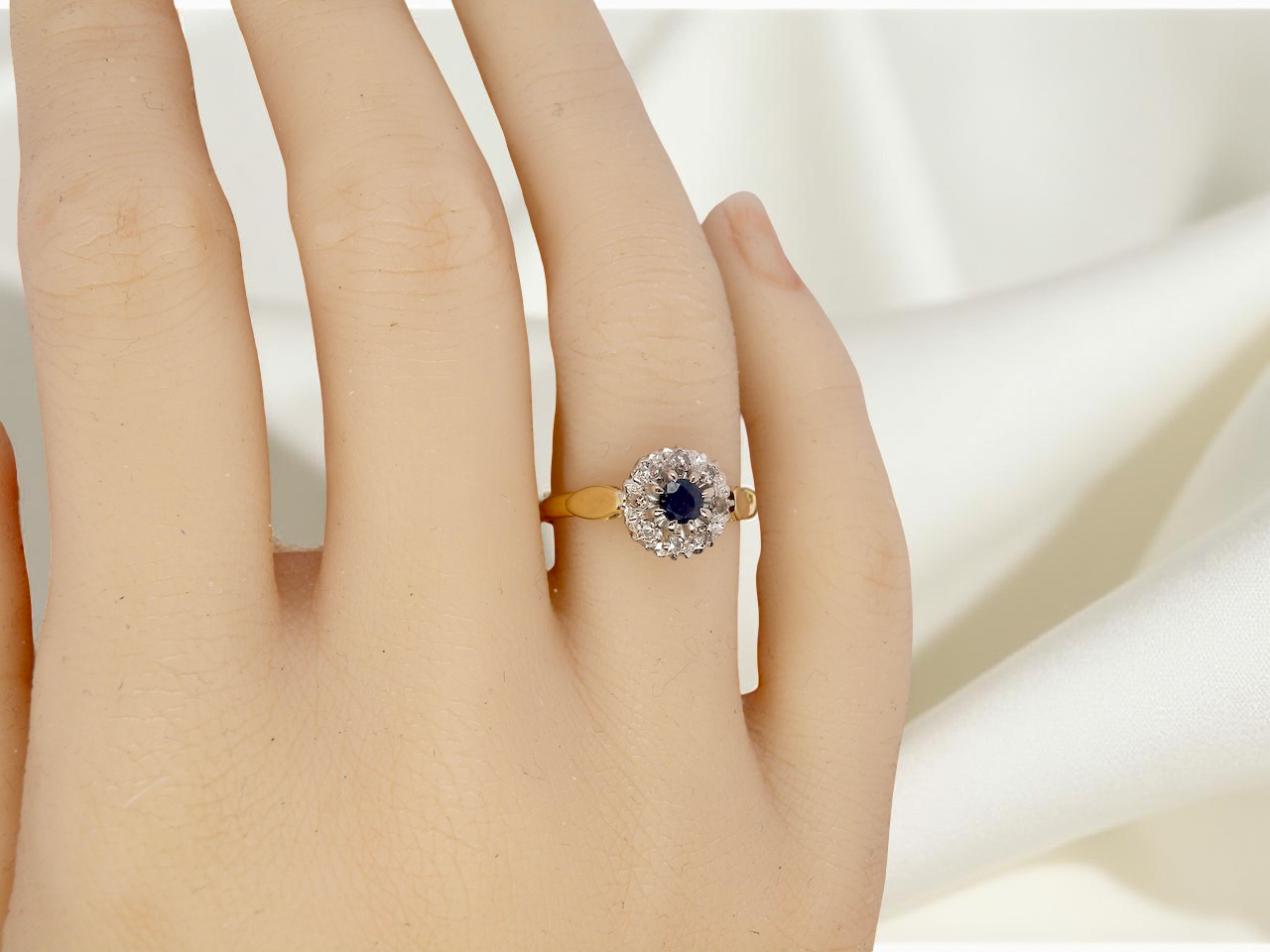 hand An 18 carat gold cluster ring, features to the centre a dark blue sapphire, 3.6mm diameter. Claw set.