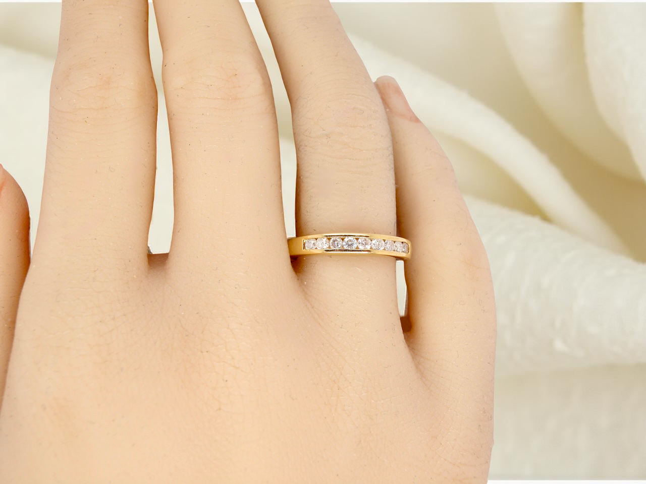 Gold ring with small diamonds on a person's finger against a soft beige background