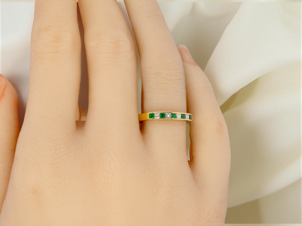 Gold ring with green gemstones on a person's finger against a soft white background