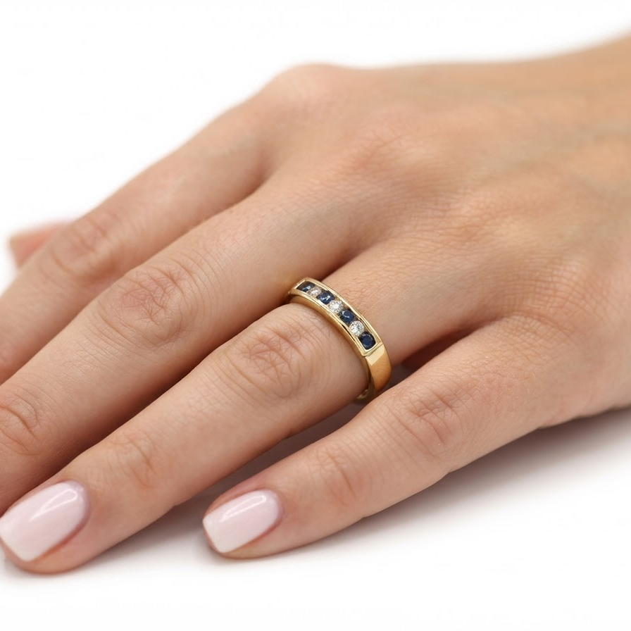 A close-up of a hand wearing a yellow gold eternity ring set with small round diamonds and dark blue round gemstones, shown against a plain white background.