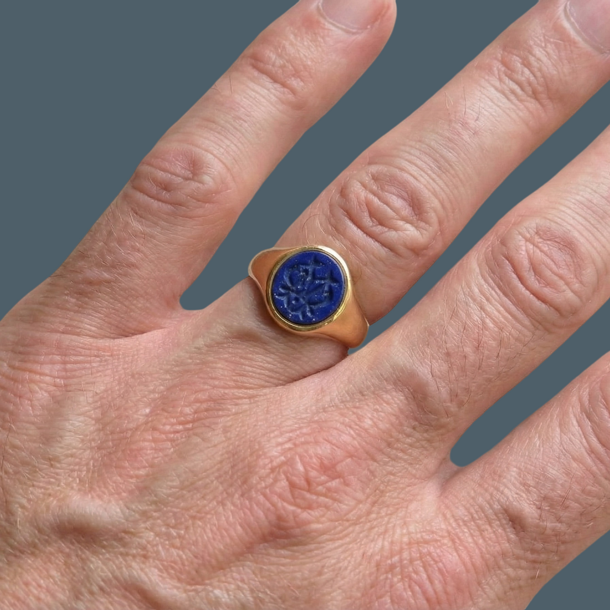 hand An 18 carat gold signet ring set with an oval lapis lazuli stone. This measures 12x9.5mm and has a carved intaglio seal engraved onto the stone. (These seem to be floral patterns)