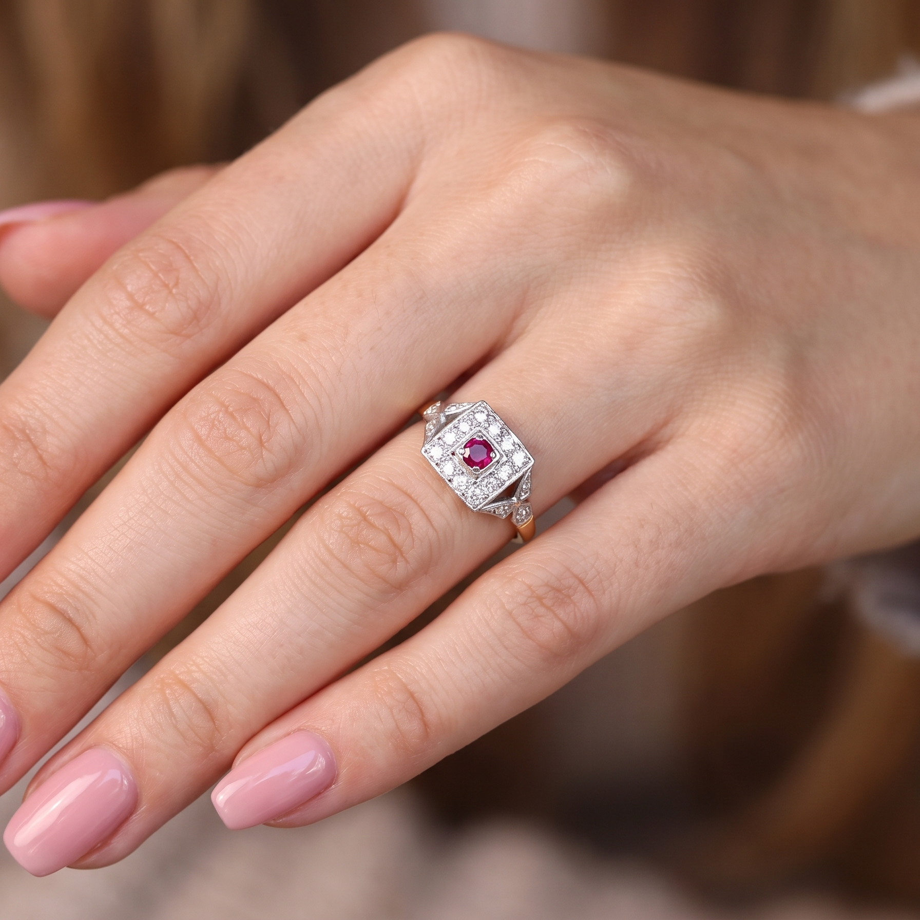 hand An 18 carat gold square cluster that features to the centre a round ruby and an outer halo of brilliant cut white diamonds.