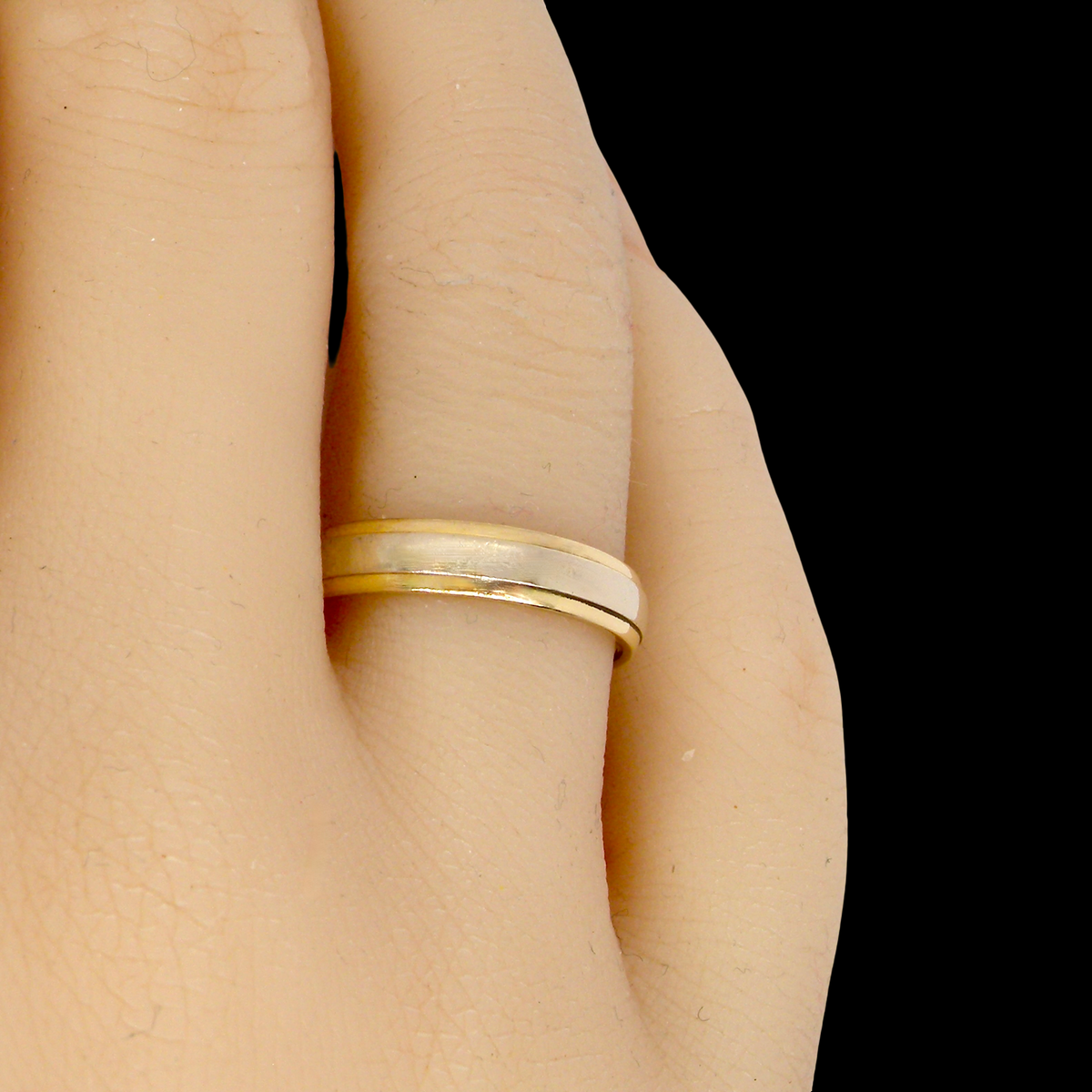 hand An 18 carat gold wedding ring. The inner band is white gold measures 2.5mm, and yellow gold narrower bands to each edge. Total width 4mm.