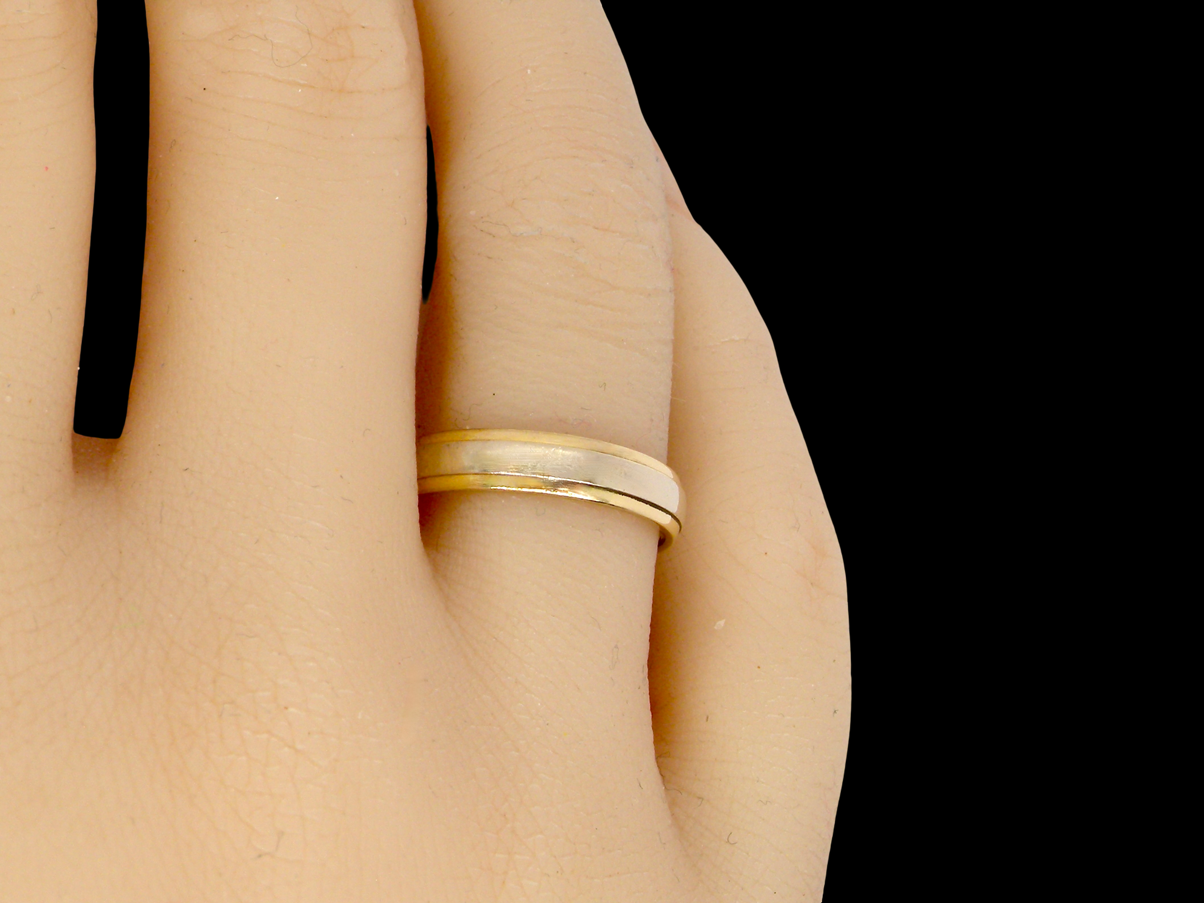 hand An 18 carat gold wedding ring. The inner band is white gold measures 2.5mm, and yellow gold narrower bands to each edge. Total width 4mm.