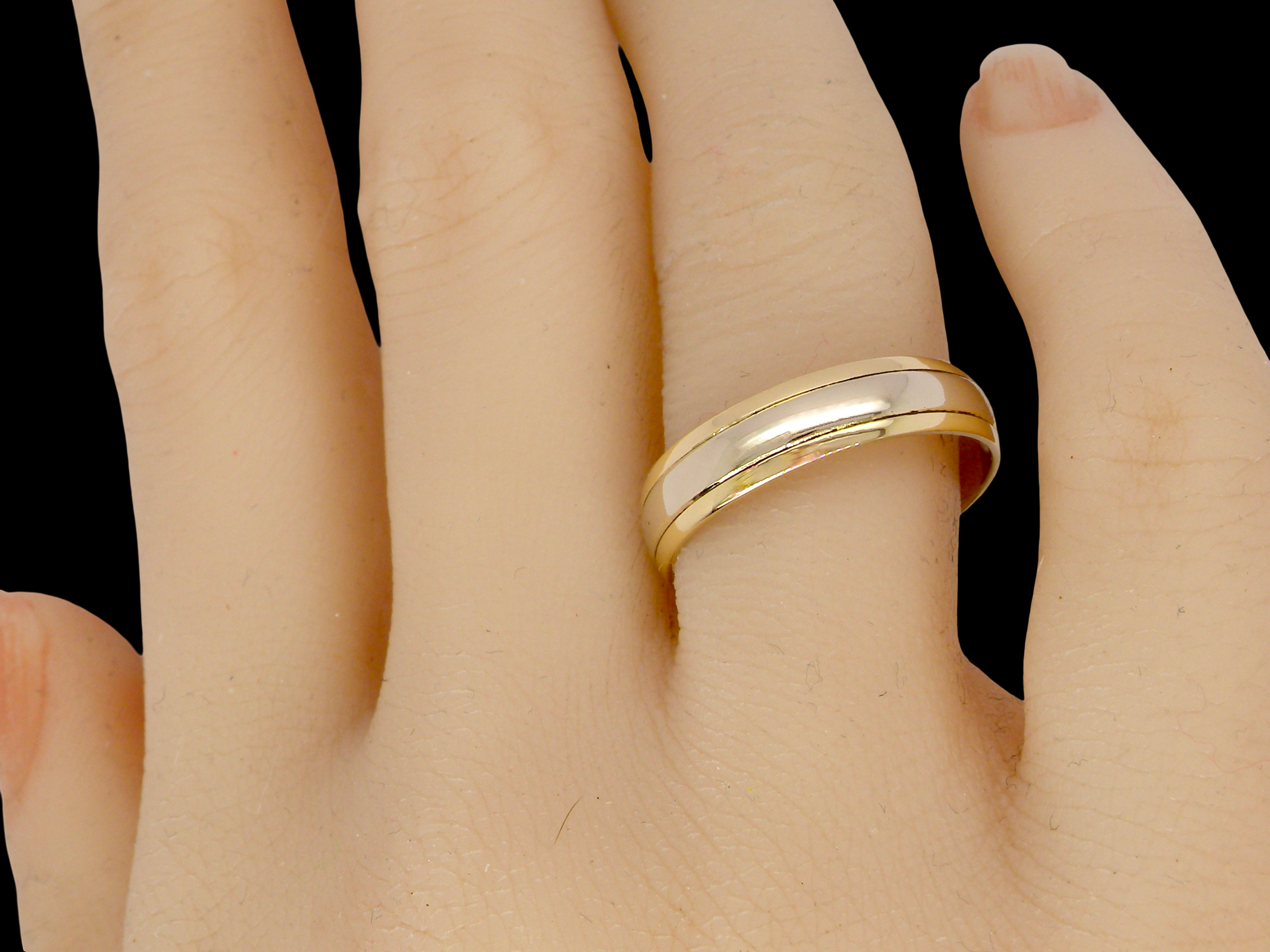hand An 18 carat gold wedding ring. The inner band is white gold measures 3.5mm, and yellow gold narrower bands to each edge. Total width 4.75mm.