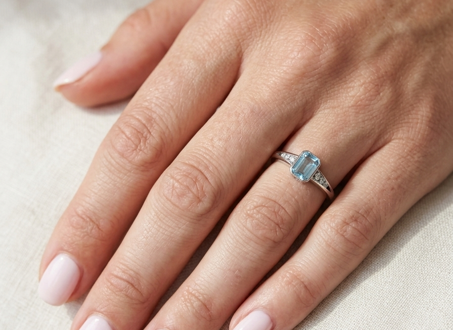 hand An 18 carat white gold ring, features a rectangular step cut aquamarine, measures 7x5mm (st one carat) sky blue, fine clarity. Rim setting.
