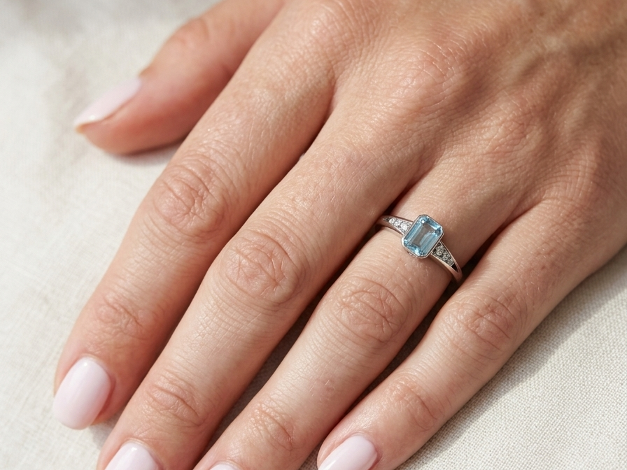 hand An 18 carat white gold ring, features a rectangular step cut aquamarine, measures 7x5mm (st one carat) sky blue, fine clarity. Rim setting.