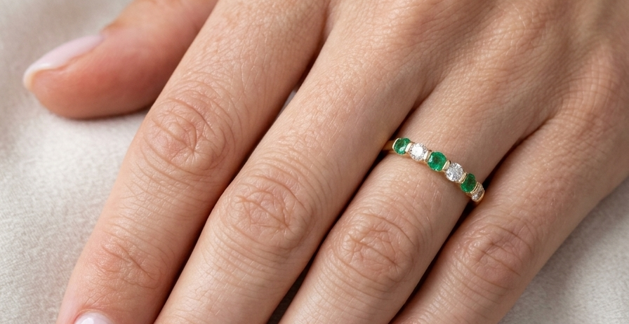 hand An 18 carat yellow gold half hoop eternity ring. Set with four bright green emeralds, each 3mm diameter (est each 0.10 carats) .