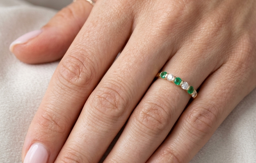 hand An 18 carat yellow gold half hoop eternity ring. Set with four bright green emeralds, each 3mm diameter (est each 0.10 carats) .