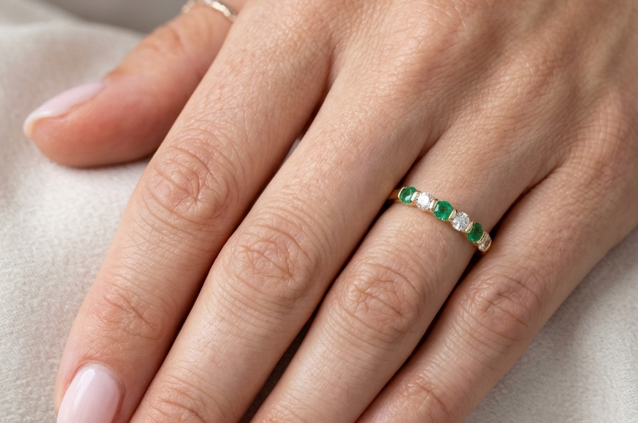 hand An 18 carat yellow gold half hoop eternity ring. Set with four bright green emeralds, each 3mm diameter (est each 0.10 carats) .
