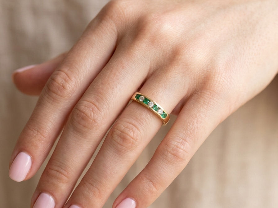 hand An 18 carat yellow gold half hoop eternity ring. Set with four round emeralds, each 3mm, and alternate set with brilliant cut white diamonds, each 3mm (total est 0.30 carats)