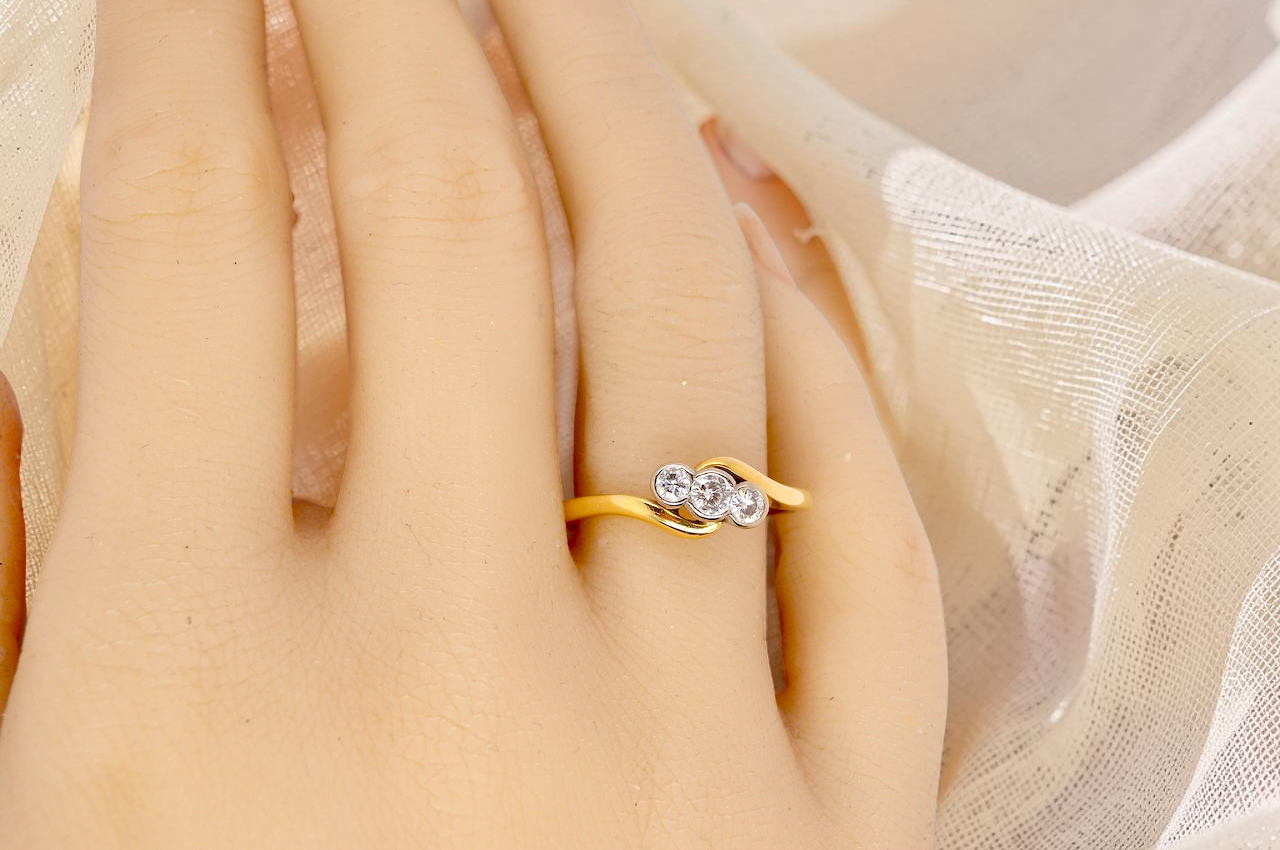 hand An 18 carat yellow gold three stone ring, cross over style, and set with brilliant cut white diamonds.
Centre stone 3mm (0.10 carats)