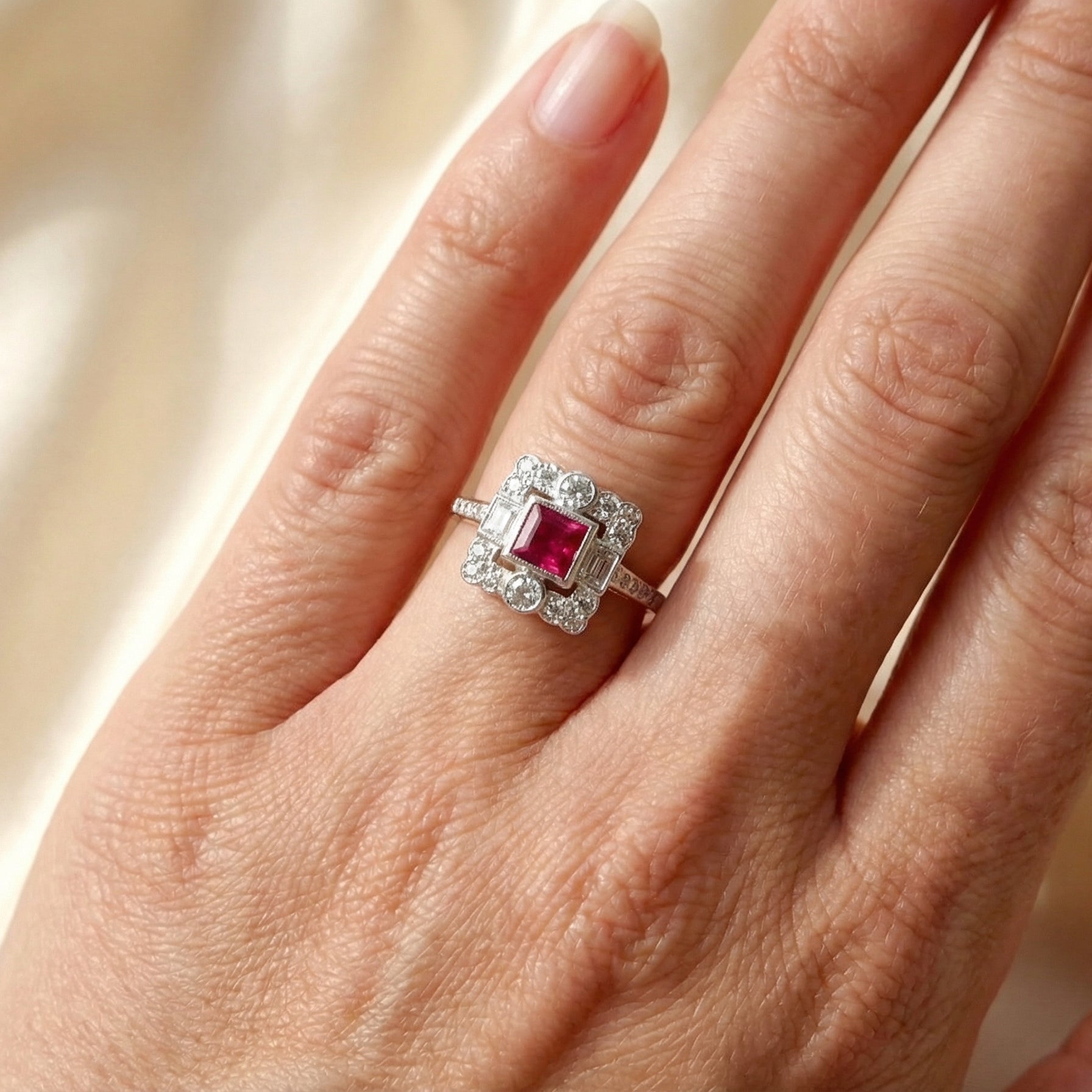 hand An Art Deco style cluster ring. Set to the centre a square 5x5mm ruby, rub over setting and complimented by a surround of mixed cut white diamonds.