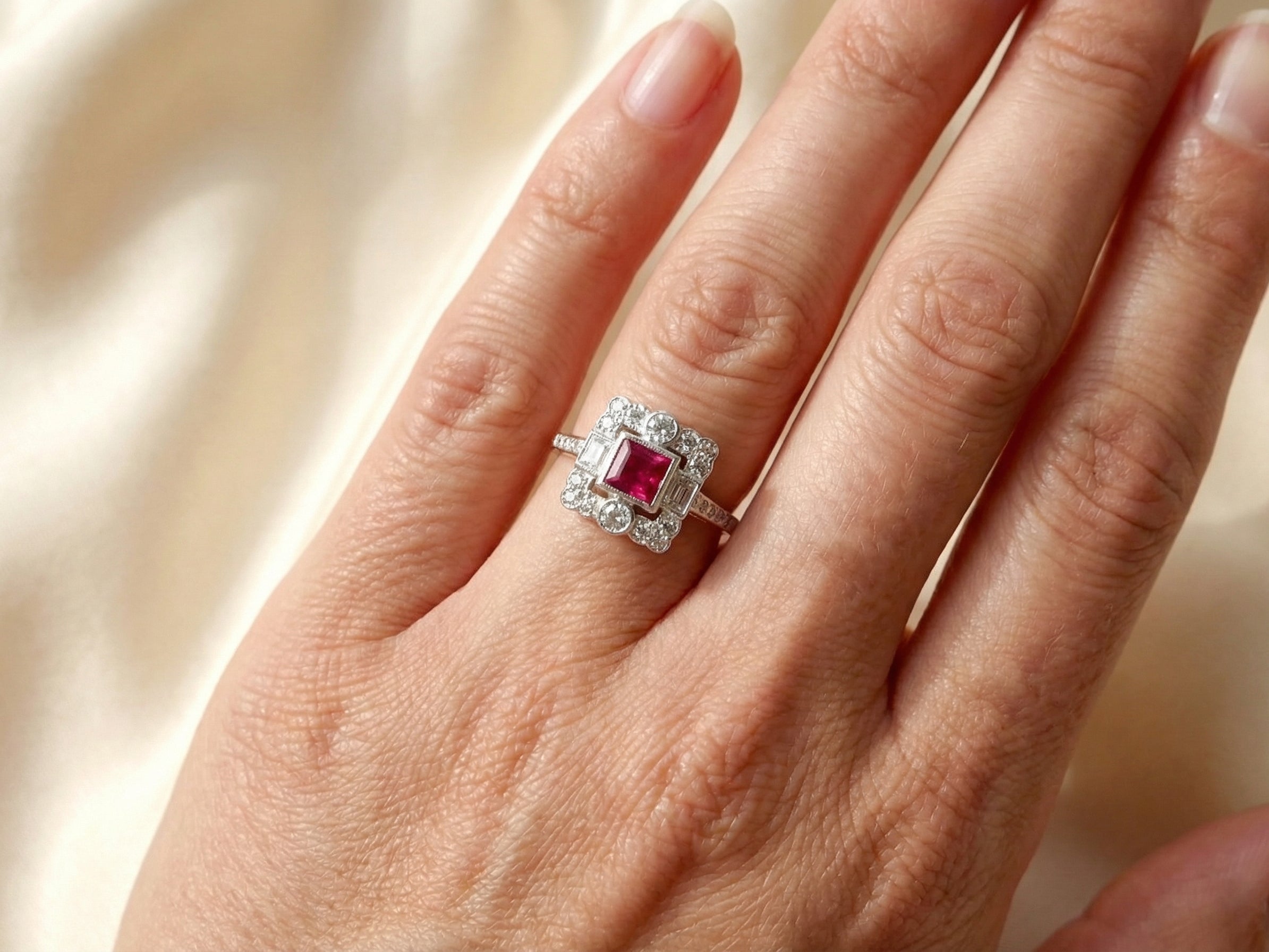 hand An Art Deco style cluster ring. Set to the centre a square 5x5mm ruby, rub over setting and complimented by a surround of mixed cut white diamonds.