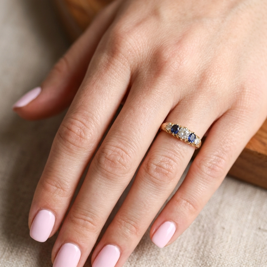 hand An antique ring from the early years of the 20th century. Centre stone 5mm diameter (0.50 carats) Colour H-j, clarity Si. Each side a mid colour blue sapphire 4mm diameter.