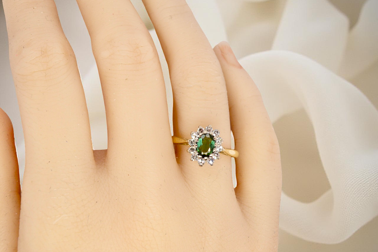hand An elegant 18 carat gold cluster ring featuring a beautifully proportioned 6 × 4mm green tourmaline