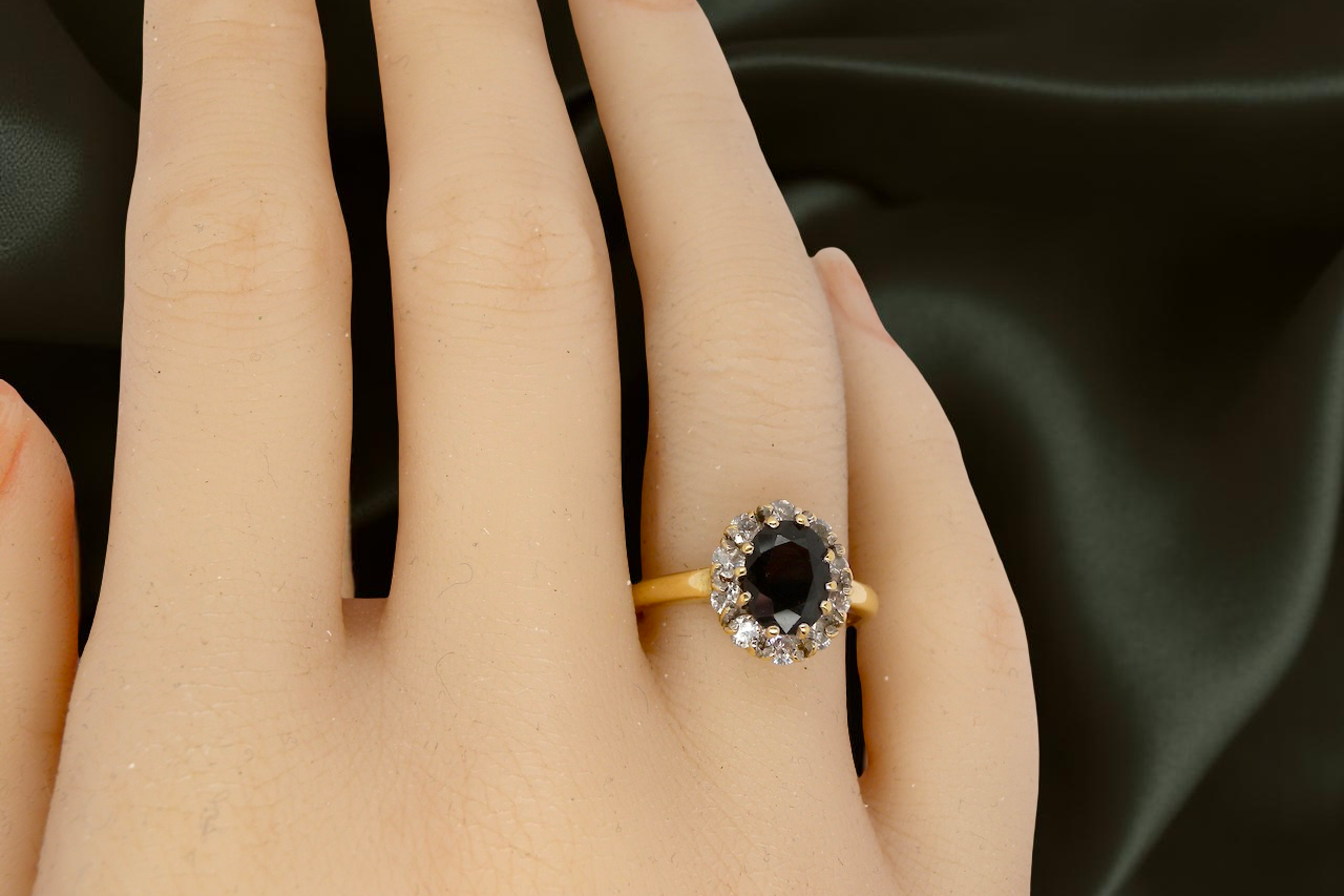 hand An elegant 18 carat gold cluster ring featuring a striking inky dark blue sapphire at its centre.