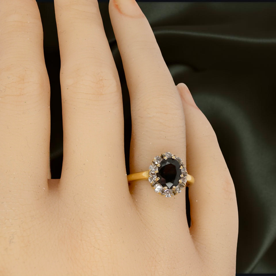 hand An elegant 18 carat gold cluster ring featuring a striking inky dark blue sapphire at its centre.