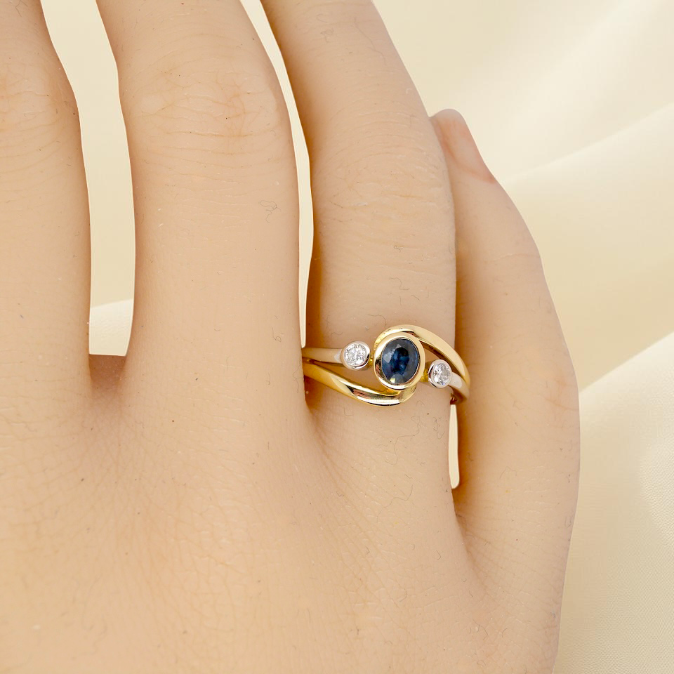 hand An elegant 18 carat gold three-stone ring featuring a rich, oval-cut dark blue sapphire at the centre, measuring 5 × 4mm, secured in a classic rim (bezel) setting.