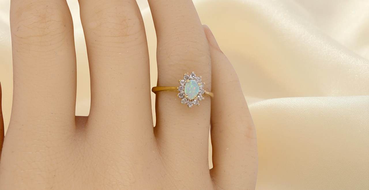 hand An elegant cluster ring featuring a white opal centre stone measuring 6 × 4mm, displaying a lively and attractive play of colour.