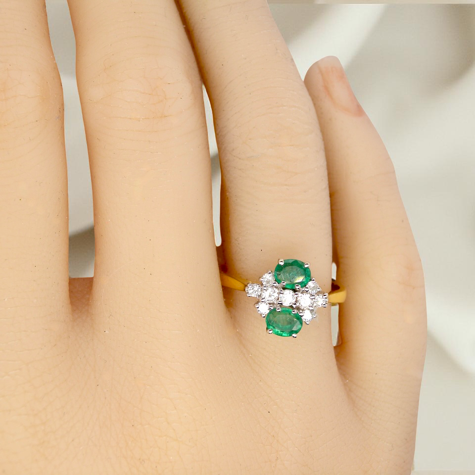 Ring with green gemstones on a person's finger against a neutral background