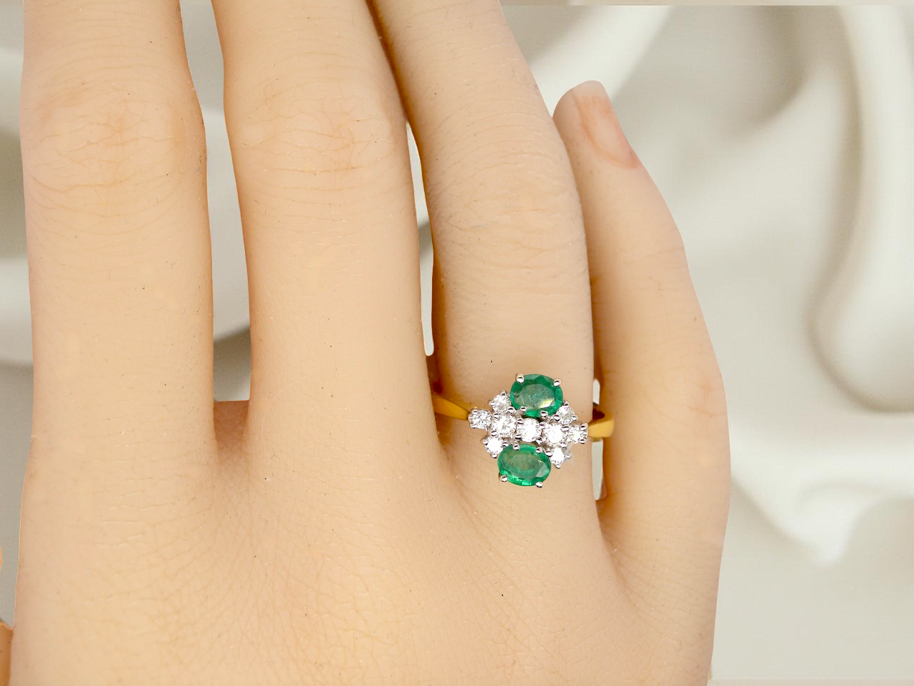 Ring with green gemstones on a person's finger against a neutral background