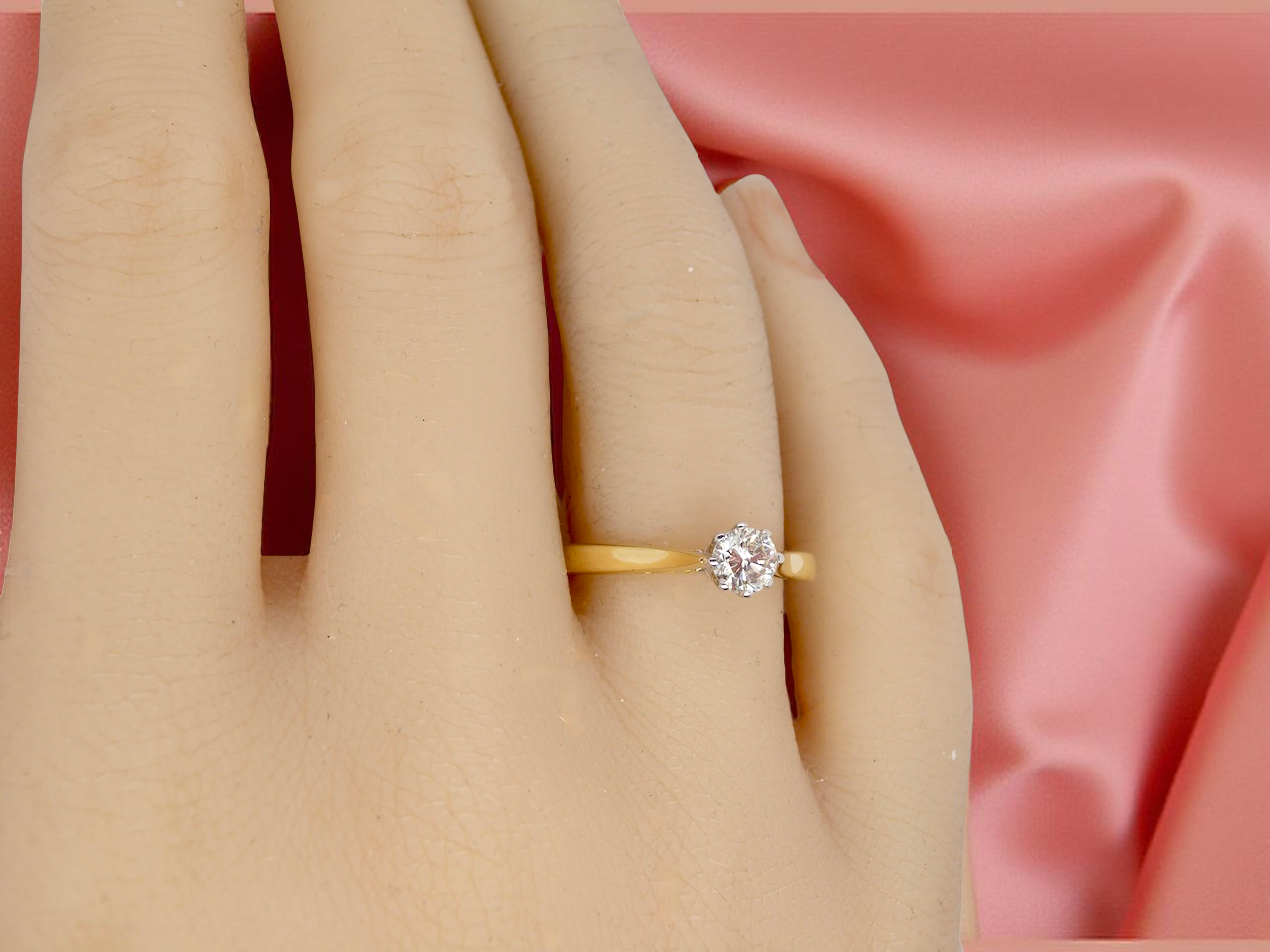 Gold ring with a diamond on a hand against a pink fabric background