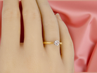 Gold ring with a diamond on a hand against a pink fabric background