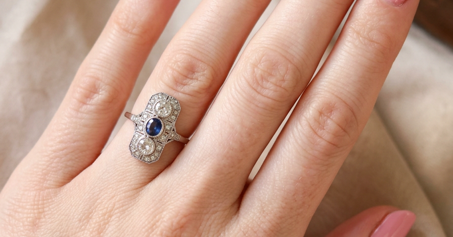 hand The plaque design has at its centre a mid to dark blue sapphire, 5x4mm (est 0.40 carats) mille grain set. Above and below to Old European Cut white diamonds. Each one estimated at 0.40 carats (4.8mm) Colour H-j, clarity Si.