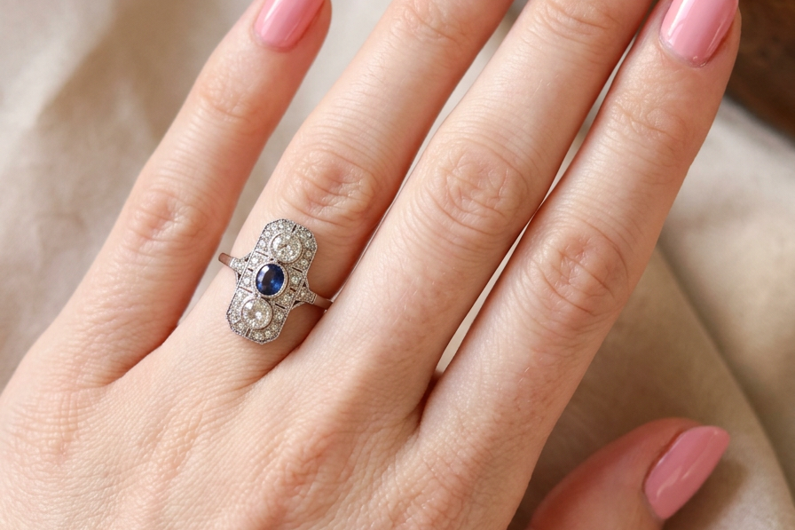 hand The plaque design has at its centre a mid to dark blue sapphire, 5x4mm (est 0.40 carats) mille grain set. Above and below to Old European Cut white diamonds. Each one estimated at 0.40 carats (4.8mm) Colour H-j, clarity Si.