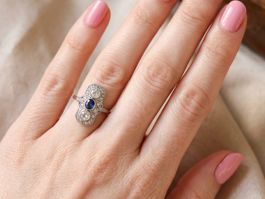 hand The plaque design has at its centre a mid to dark blue sapphire, 5x4mm (est 0.40 carats) mille grain set. Above and below to Old European Cut white diamonds. Each one estimated at 0.40 carats (4.8mm) Colour H-j, clarity Si.