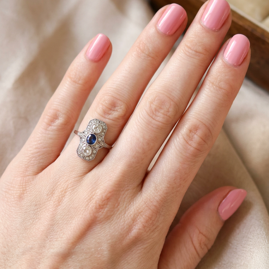 hand The plaque design has at its centre a mid to dark blue sapphire, 5x4mm (est 0.40 carats) mille grain set. Above and below to Old European Cut white diamonds. Each one estimated at 0.40 carats (4.8mm) Colour H-j, clarity Si.
