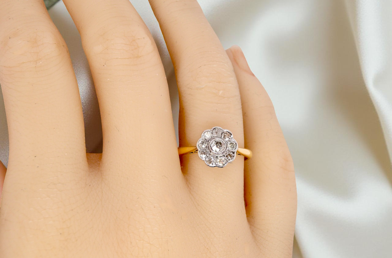 hand early 20th-century vintage diamond cluster ring, featuring a classic daisy-shaped head set with nine old brilliant-cut white diamonds.